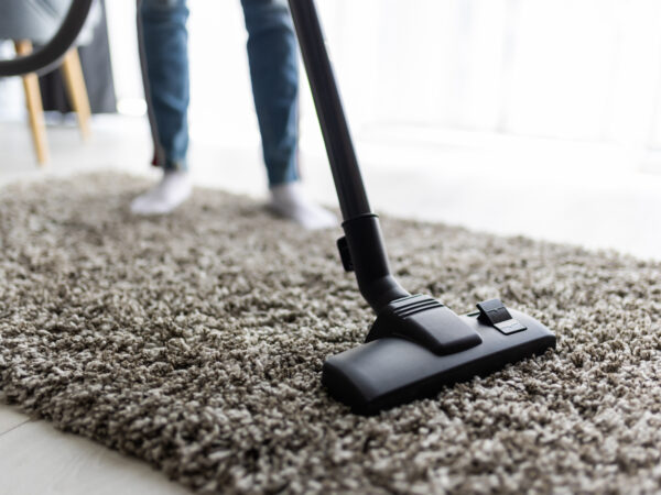 people, housework and housekeeping concept – close up of woman with legs vacuum cleaner cleaning carpet at home Close up of woman with legs vacuum cleaner cleaning carpet at home