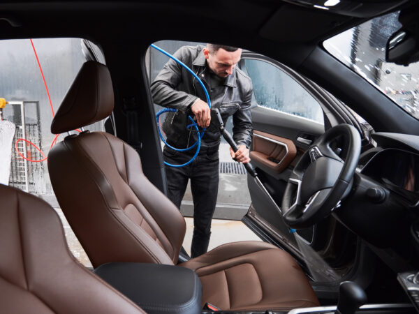 Young man washing car on carwash station outdoor View from inside a car on young man washing car on carwash station outdoor. Handsome driver cleaning automobile, using high pressure water.